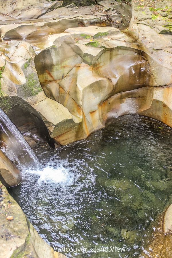A small waterfall dropping from a uniquely carved rock bed into a deep turqouise coloured pool. This is the Cumberland Potholes found near Cumberland, BC on Vancouver Island. Vancouver Island View