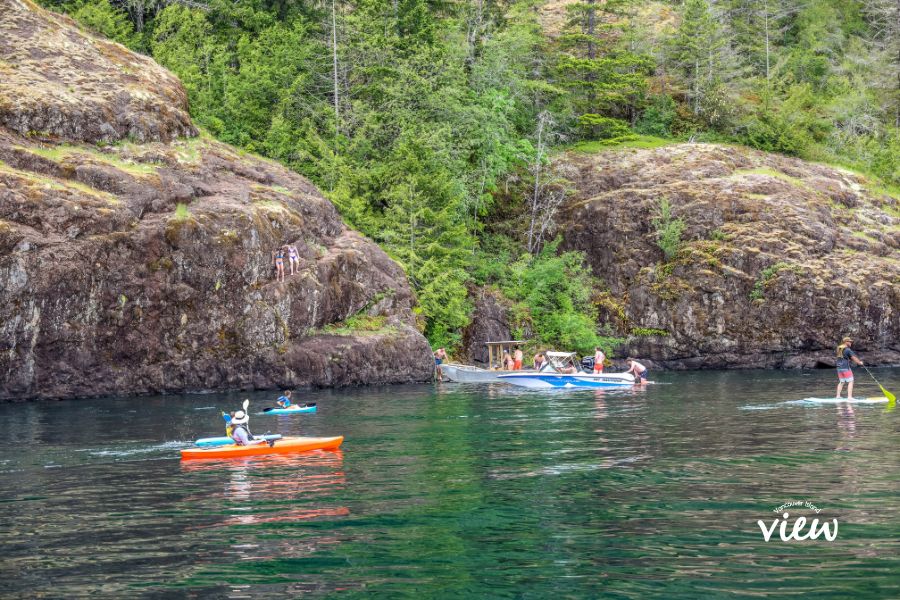 People swimming, kayaking and boating against a large rocky backdrop on Sproat Lake in Port Alberni during the summer. Vancouver Island weather. Vancouver Island View.